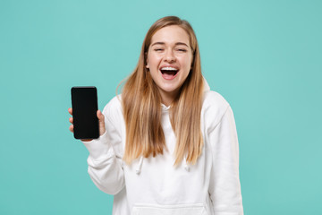 Fototapeta premium Laughing young woman girl in casual white hoodie posing isolated on blue turquoise background studio portrait. People lifestyle concept. Mock up copy space. Hold mobile phone with blank empty screen.