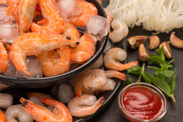 Tiger prawns and shrimp in black plate with ice. Tomato sauce, mint, garlic.