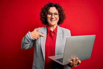 Middle age curly hair business woman working using laptop over isolated red background with surprise face pointing finger to himself