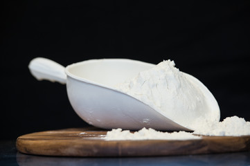 flour put on a wooden board and sprinkles from the scoop with a black background