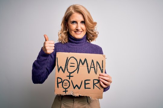 Middle age beautiful blonde woman asking for women rights holding banner happy with big smile doing ok sign, thumb up with fingers, excellent sign