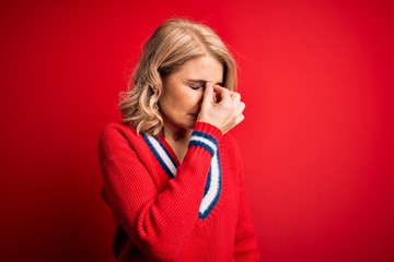 Middle age beautiful blonde woman wearing casual sweater over isolated red background tired rubbing nose and eyes feeling fatigue and headache. Stress and frustration concept.