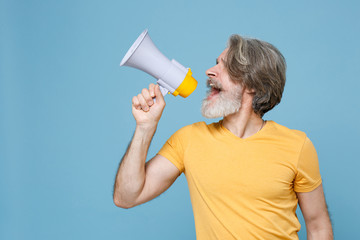 Elderly gray-haired mustache bearded man in casual yellow t-shirt posing isolated on blue wall background in studio. People lifestyle concept. Mock up copy space. Scream in megaphone looking aside up.