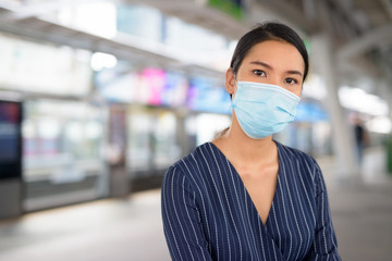 Face of young Asian businesswoman with mask for protection from corona virus outbreak at the skytrain station