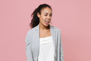 Fototapeta premium Cheerful funny young african american business woman in grey suit white shirt posing isolated on pink background in studio. Achievement career wealth business concept. Mock up copy space. Blinking.