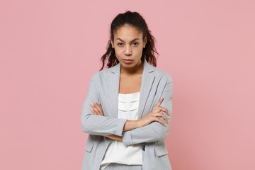 Concerned young african american business woman in grey suit white shirt posing isolated on pink wall background studio portrait. Achievement career wealth business concept. Holding hands crossed.