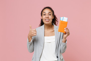 Smiling young african american business woman in grey suit white shirt isolated on pink background. Achievement career wealth business concept. Hold passport tickets boarding pass, showing thumb up.