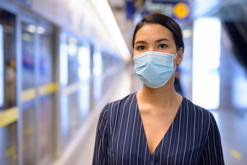 Young Asian businesswoman with mask for protection from corona virus outbreak waiting at the subway train station