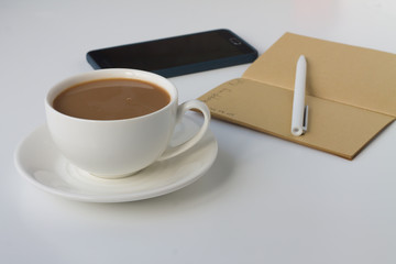 A cup of coffee with milk and a notebook with a pen on a white background