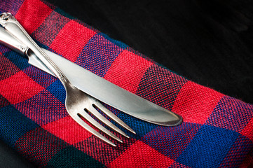 Close up of a vintage silver knife and fork on red blue napkin on a dark concrete table, horizontal image