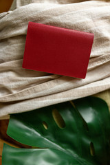 A red notebook is lying on a beige cloth, next to a green leaf. Space for text
