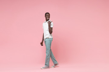 Side view of smiling young african american man guy in white polo shirt, turquoise trousers posing...