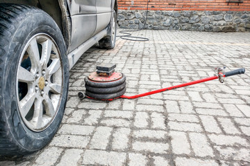 A pneumatic jack is lying on a tile floor next to a dusty black car in a car repair shop