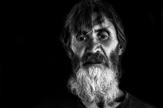 Dramatic close up black and white portrait of old homeless alcoholic man face with white beard depressed sick and lonely, social issues documentary concept with hard contrast