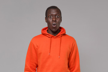 Shocked young african american man guy in orange streetwear hoodie posing isolated on grey background studio portrait. People sincere emotions, lifestyle concept. Mock up copy space. Looking camera.