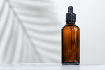 Creative photo of cosmetic bottle with pipette on a white background with shadow of tropical...
