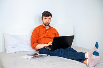 Serious man working at home using laptop and headset on bed