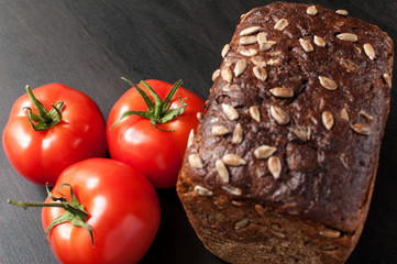 delicious fresh baked bread with bran sunflower seeds and a few fresh tomatoes on a dark kitchen table, horizontal image