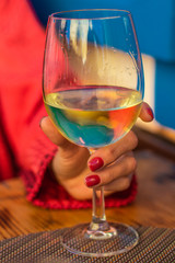 Adult hand holding glass of white whine on the table. Toasting at celebration . Cozy cafe or restaurant background outdoors. Concept of enjoyment, happiness and party.