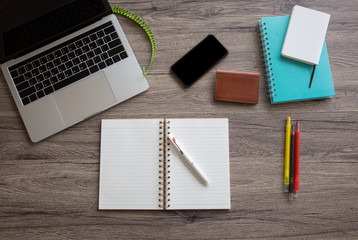 A top view of a business desk with opening blank book includes color pens, notebook, business card bag, computer laptop and smartphone on a wooden table to connect with others in the digital world.