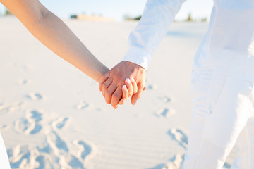 Lovers hold hands and walk in the white desert