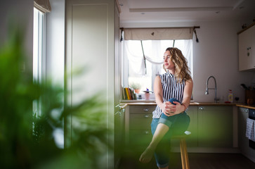Young woman sitting in kitchen indoors at home, relaxing.
