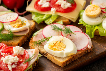 Toasts with eggs, cheese, ham, radish, cucumbers and tomatoes , breakfast idea.