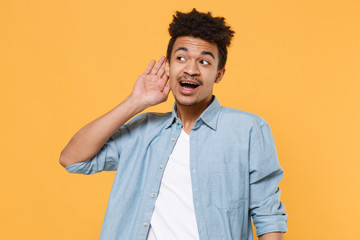 Curious young african american guy in casual blue shirt posing isolated on yellow background studio...