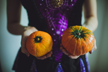 A girl in a festive dress holding pumpkins for Halloween.