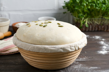 Homemade freshly prepared yeast dough in a basket for baking with pampkin seeds on a dark wooden background.