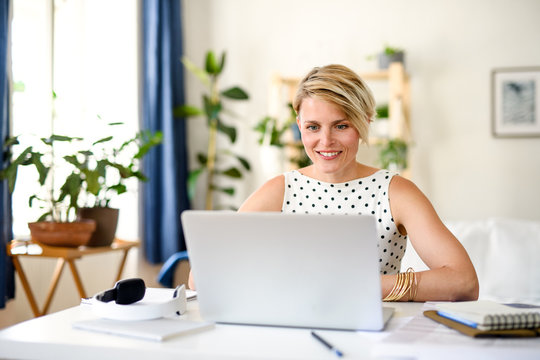Cheerful young businesswoman with laptop indoors in home office, working.