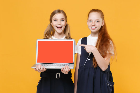 Two girls 12-13 years old in white t-shirt blue school uniform hold laptop pc computer isolated on yellow background children studio portrait Childhood education lifestyle concept Mock up copy space