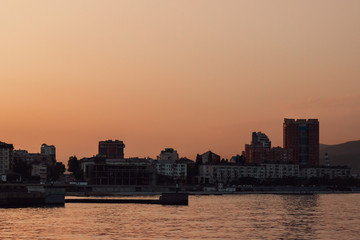 Naklejka premium Summer sunset on the sea cost. City skyline in golden hour (orange color treatment). 