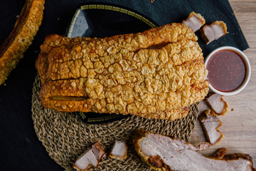 Large crispy pork on a black plate, cut into slices on a wooden chopping board with spicy sauce on a wooden table