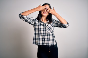 Young brunette woman with blue eyes wearing casual shirt and glasses over white background covering eyes with hands smiling cheerful and funny. Blind concept.