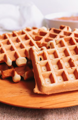 Belgian waffles on wooden plate on a table and sosket with jam behind
