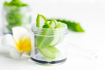 Slices of natural organic aloe vera plant in jar for homemade cosmetic lotion or oil against white background.