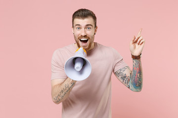 Excited young bearded tattooed man guy in pastel casual t-shirt posing isolated on pink background studio. People lifestyle concept. Mock up copy space. Scream in megaphone, pointing index finger up.