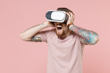 Shocked young bearded tattooed man guy in pastel casual t-shirt posing isolated on pink background studio portrait. People lifestyle concept. Mock up copy space. Watching in headset put hands on head.