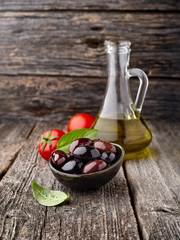 Olives with basil leaves, tomatoes and olive oil on a wooden background.