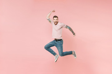 Fototapeta na wymiar Excited young tattooed man guy in pastel casual t-shirt posing isolated on pink background studio portrait. People sincere emotions lifestyle concept. Mock up copy space. Jumping doing winner gesture.