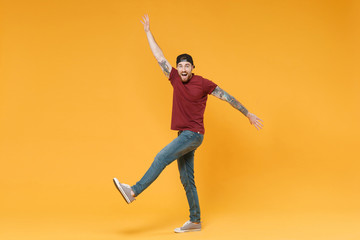Excited young bearded tattooed man guy in casual t-shirt black cap posing isolated on yellow wall background studio portrait. People lifestyle concept. Mock up copy space. Spreading hands and legs.
