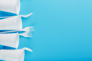 Plastic tableware on a blue background. Disposable forks and glasses with free space.