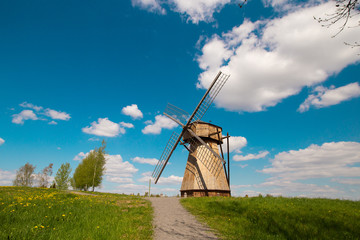 Old ancient historical windmill in countryside village. Pleasant sunny weather, blue sky, white clouds, green trees and scenery view