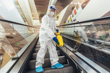 Professional workers in hazmat suits disinfecting indoor of mall, pandemic health risk, coronavirus