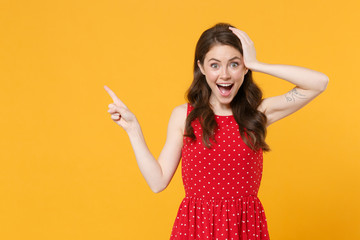 Excited young brunette woman girl in red summer dress posing isolated on yellow background studio portrait. People lifestyle concept. Mock up copy space. Pointing index finger aside put hand on head.