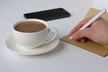 A cup of coffee with milk and a notebook with a pen on a white background