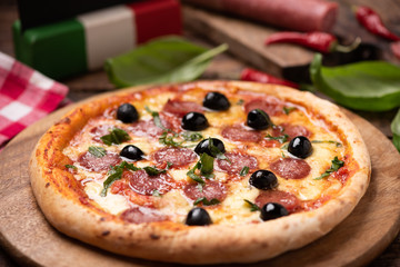 Delicious fresh oven baked spicy salami or pepperoni pizza with melted cheese and olives on a wooden board