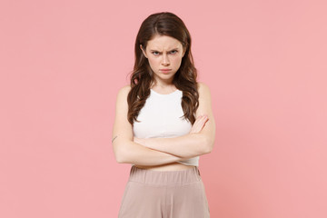 Fototapeta premium Offended young brunette woman girl in light casual clothes posing isolated on pastel pink wall background studio portrait. People emotions lifestyle concept. Mock up copy space. Holding hands crossed.