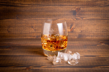 Glass of whiskey and ice cubes on a wooden background